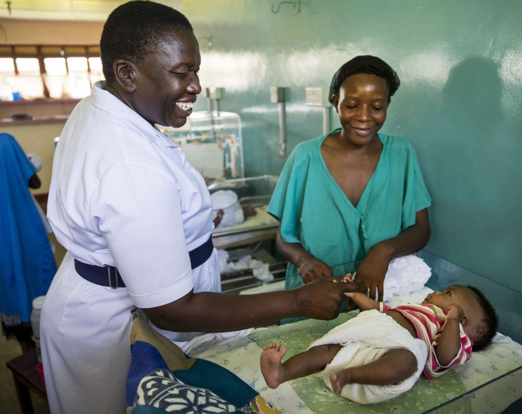 A nurse smiles with a baby as mother looks on. Adara Group photo.